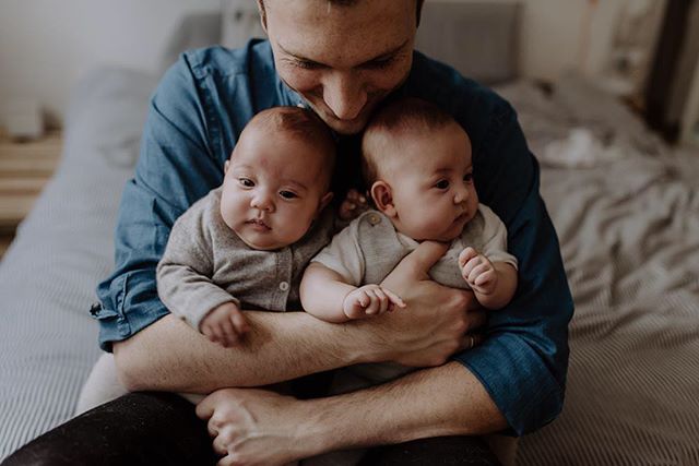 A father lovingly holds his newborn twins in a cozy indoor setting, bonding with his babies.