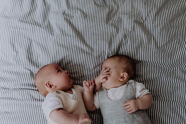 Two adorable baby twins lie on a striped blanket, creating a tender and loving scene.