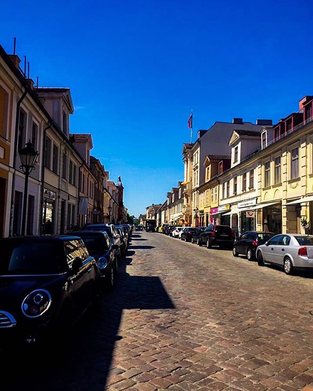 A street lined with parked cars and historic buildings under a clear blue sky.