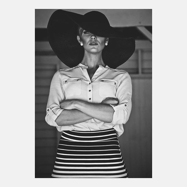 Elegant woman in a hat and striped skirt strikes a confident pose in this black and white fashion shot.