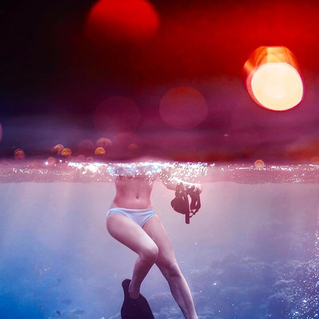 A woman stands in the ocean, partially submerged, wearing diving fins and holding a mask.