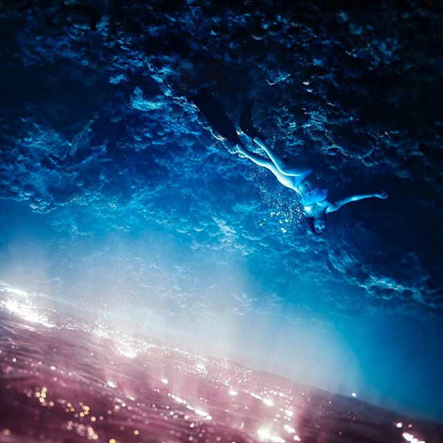 A lone woman swims underwater in a dreamlike ocean scene with ethereal lighting, highlighting the beauty of aquatic wellness.