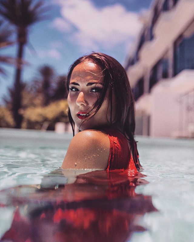A woman in a red swimsuit relaxes in a pool on a sunny day, enjoying a peaceful moment in the water.