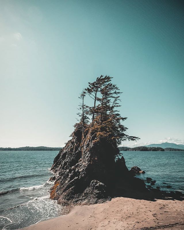 A tranquil seascape featuring a rocky island with trees, surrounded by the ocean under a clear sky.