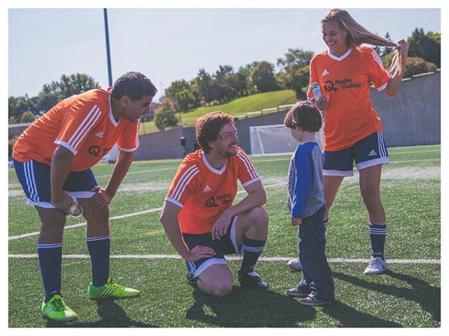A group wearing orange soccer jerseys is gathered on a soccer field on a sunny day.