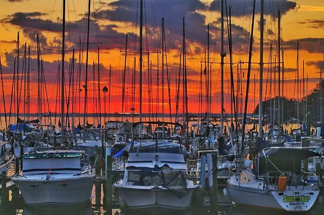 A tranquil marina scene at sunset, featuring sailboats and yachts with a colorful sky.