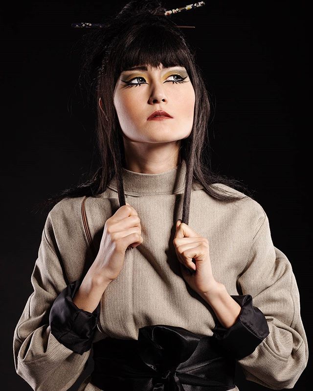Elegant woman with artistic makeup and hairstyle poses in a studio setting.
