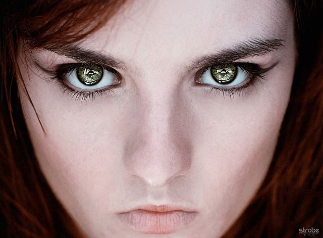 A close-up of a woman's face with intense green eyes and bold eyeliner, captured in editorial style.
