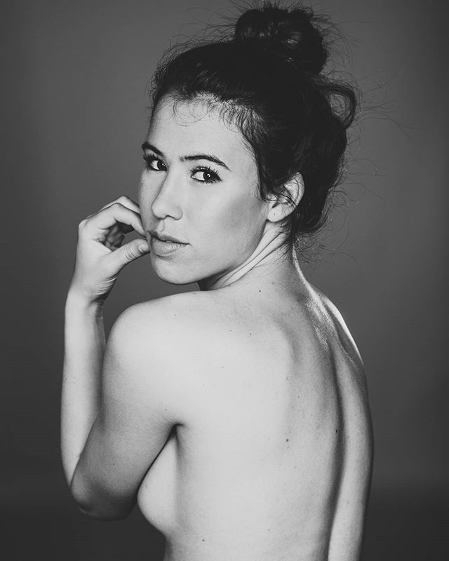 Black and white portrait of a sensual woman in a studio setting, looking over her shoulder.
