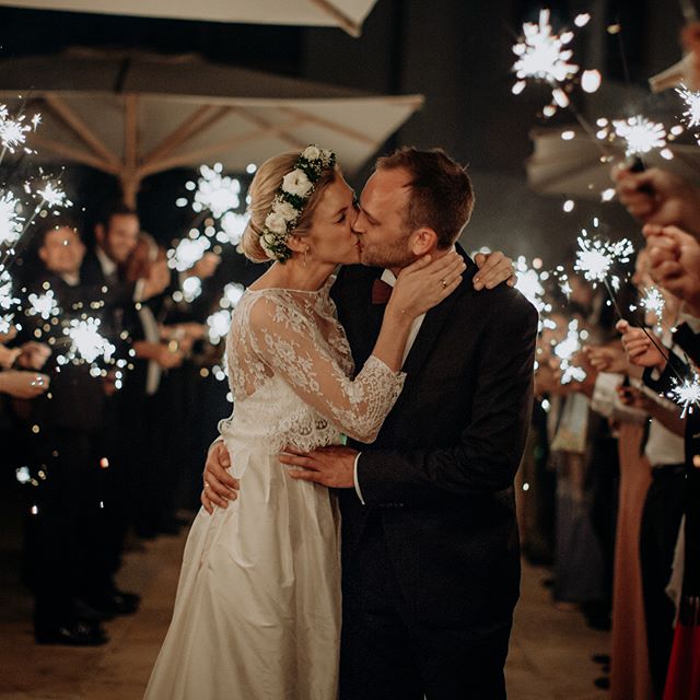 Newlyweds share a kiss surrounded by guests with sparklers at their wedding reception.