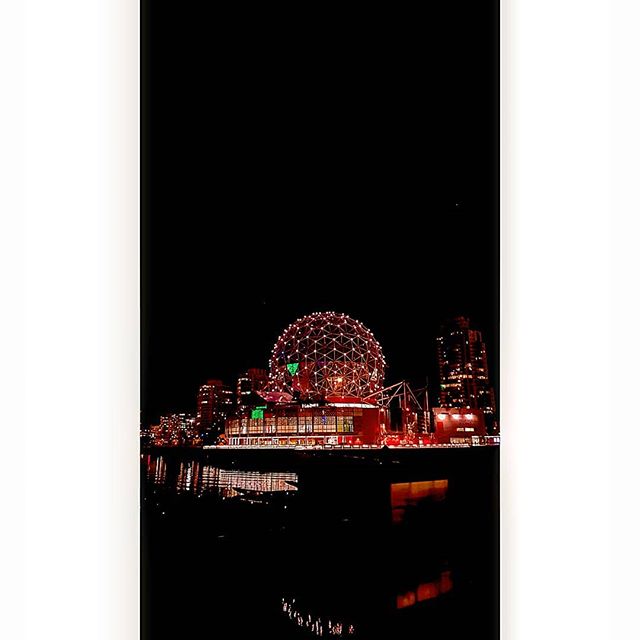 Vancouver's Science World glows at night, reflected in the calm water, showcasing the city's vibrant skyline.