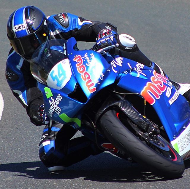 A motorcyclist leans into a turn on a bright blue motorcycle at the racetrack.