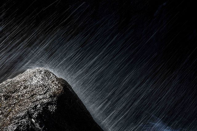 A dark, long exposure shot shows water cascading over a rough rock, creating a dynamic and abstract natural scene.