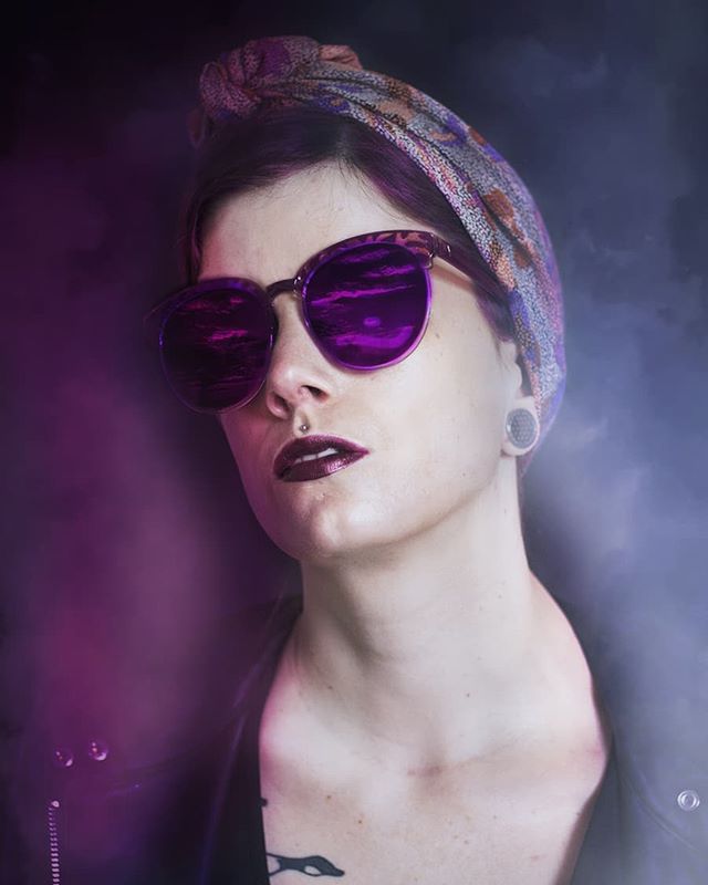 Stylish woman with sunglasses and a headband poses in a studio setting with moody lighting.