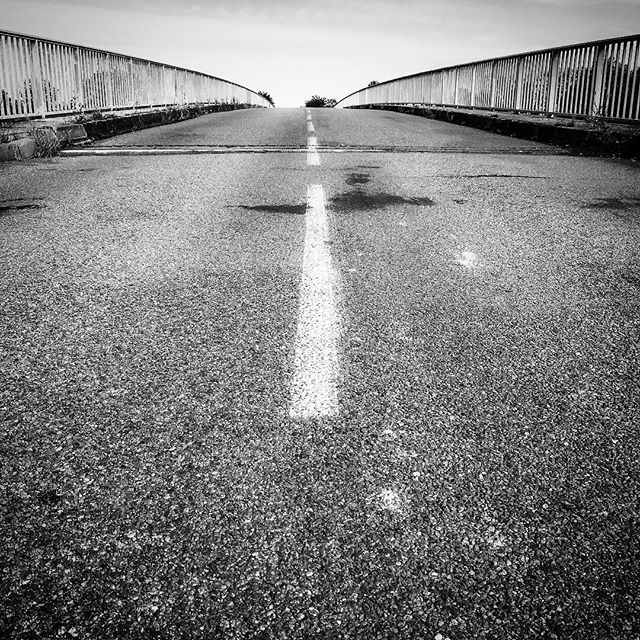 A black and white shot of a road and bridge, focusing on the ground and white road line.