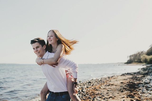 A young couple piggybacking on a sandy beach, enjoying a cheerful and playful moment by the sea on a sunny day.