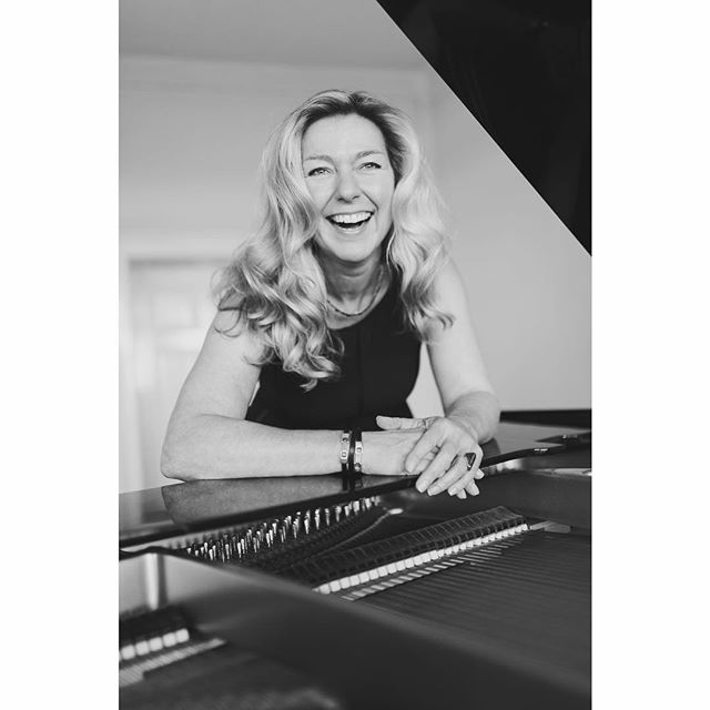 A joyful woman at a piano, smiles in this black and white image.