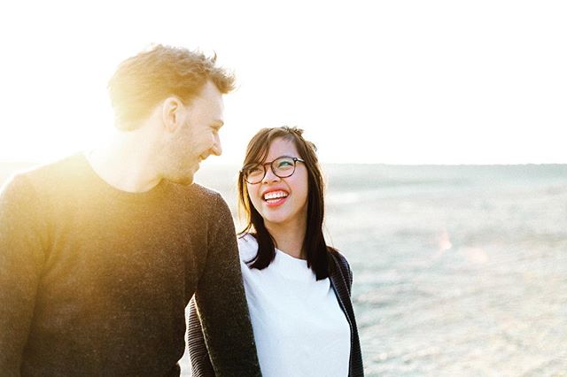 A smiling couple enjoys a romantic walk on the beach at sunset. They look affectionately at each other.