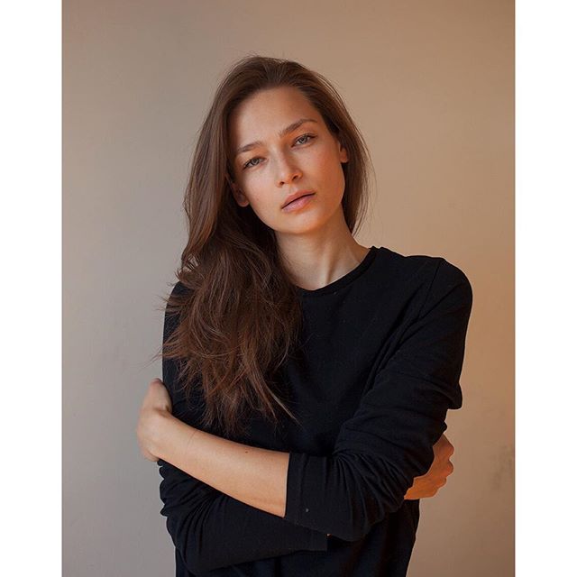 A young woman with long brown hair poses indoors with a calm and serene expression, perfect for skincare campaigns.