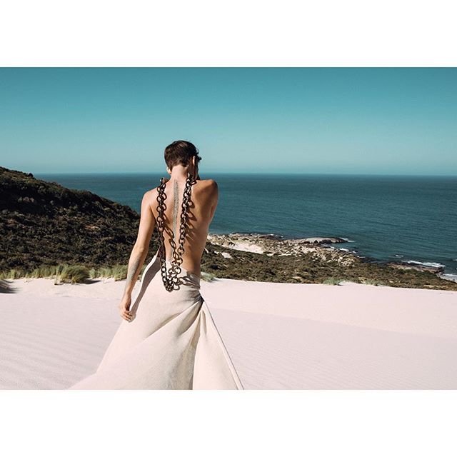 A man stands on a sandy dune overlooking the ocean in a serene, artistic setting.
