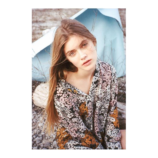 A young woman with long hair poses outdoors in a floral dress, creating a dreamy and serene atmosphere.