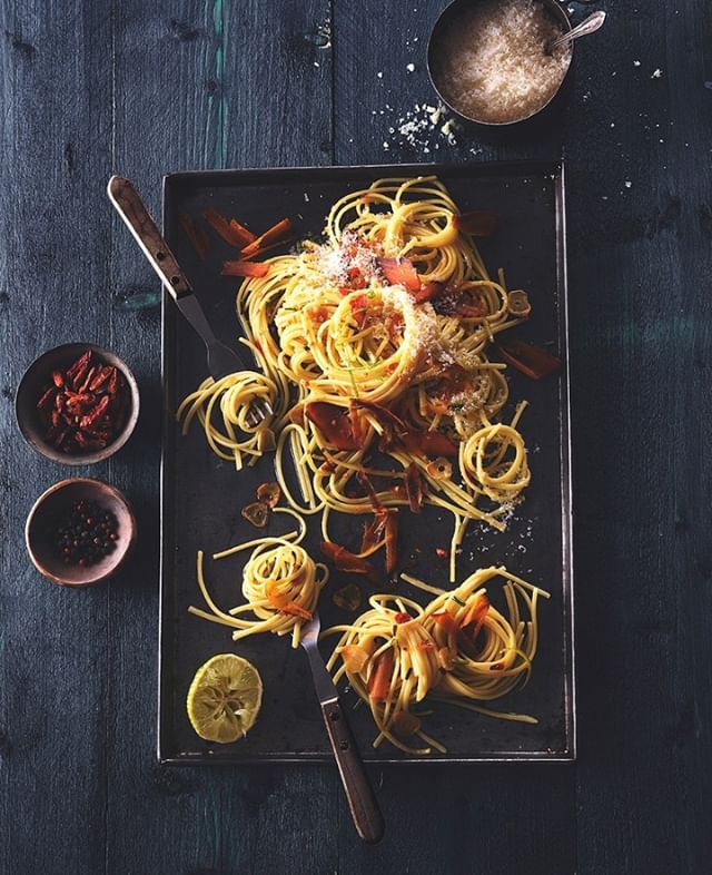 Overhead shot of spaghetti with tomatoes, parmesan and lemon on a rustic dark surface. 