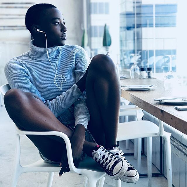 A stylish woman sits by a bright window listening to music on her headphones in a modern cafe.