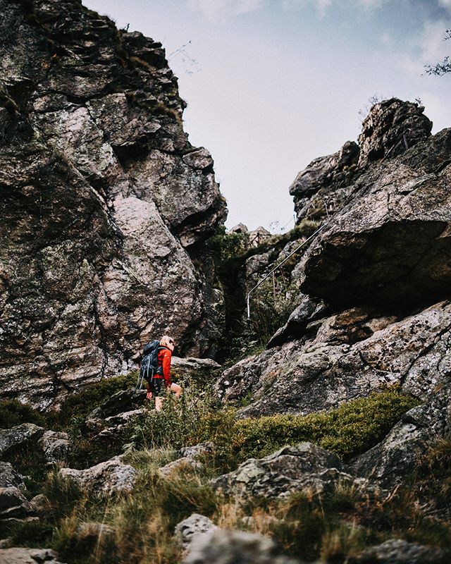 A woman hikes through a rocky mountain landscape wearing a backpack.