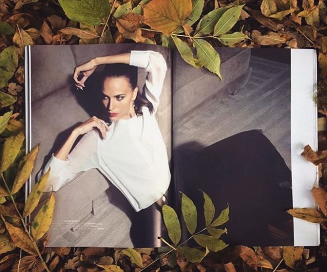 A stylish woman in a magazine lays on fallen leaves in an outdoor fashion editorial.