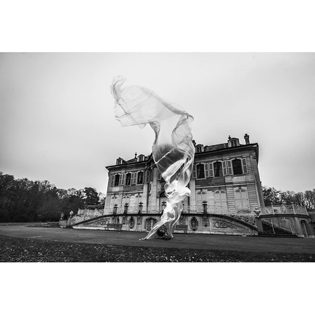 A woman dances with flowing fabric in front of a historic estate, captured in elegant monochrome.