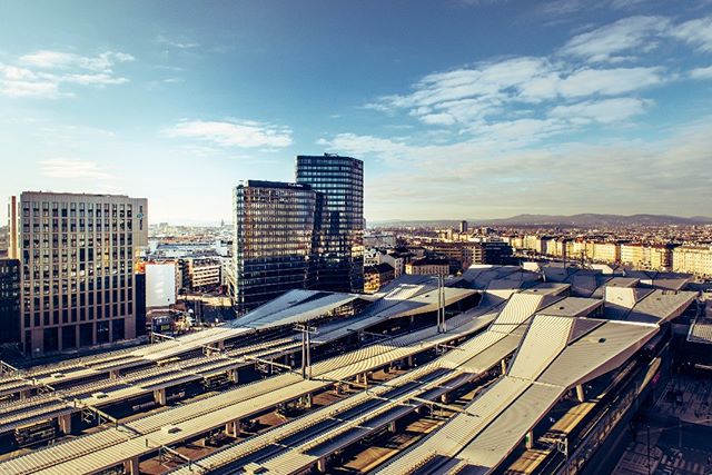 A cityscape view featuring modern architecture and a train station, under a blue sky with scattered clouds.