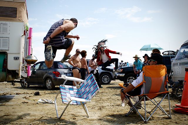 People enjoy activities at an outdoor event in the desert with vehicles and camping equipment.