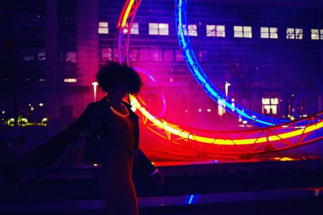 A woman walks at night with colorful light installations in an urban setting.