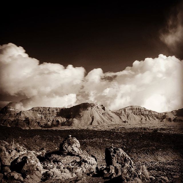 Sepia toned landscape featuring mountains, clouds, and a rocky terrain.