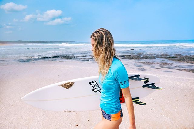 A surfer walks on the beach carrying her board near the ocean.