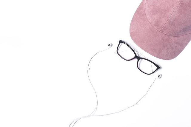 Pink cap, black glasses, and earphones arranged on a clean white surface in a flat lay composition.