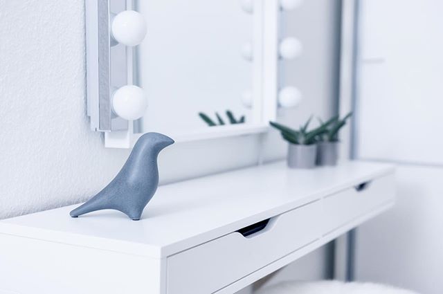 A simple makeup vanity with a bird figurine and soft lighting creates a serene, modern atmosphere for beauty and self-care.