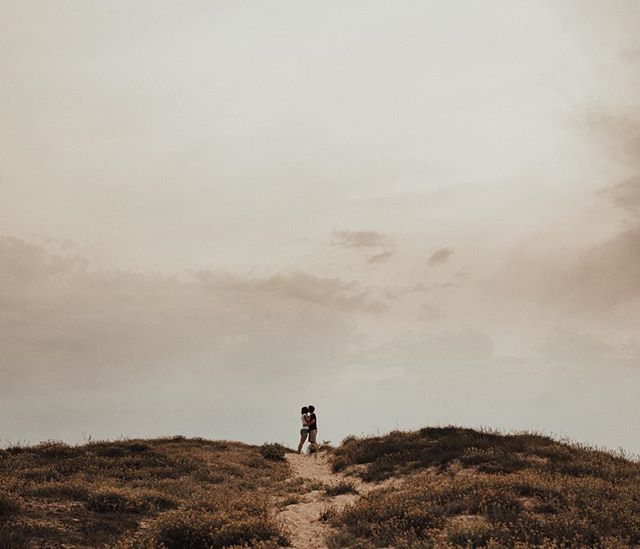 A couple embraces on a hilltop under an overcast sky, capturing a moment of intimacy and calm in nature.