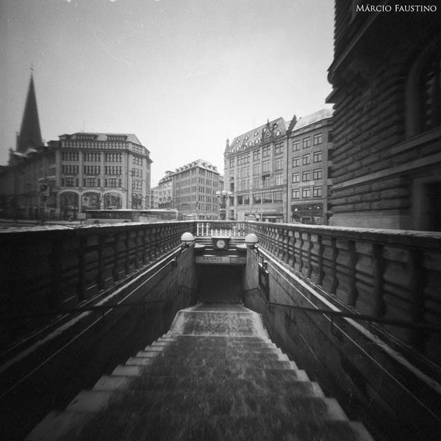 A vintage black and white image captures a city street with buildings and a subway entrance.
