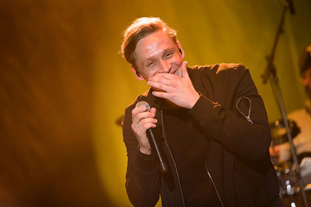 A joyful male singer performs on stage with a microphone in hand.