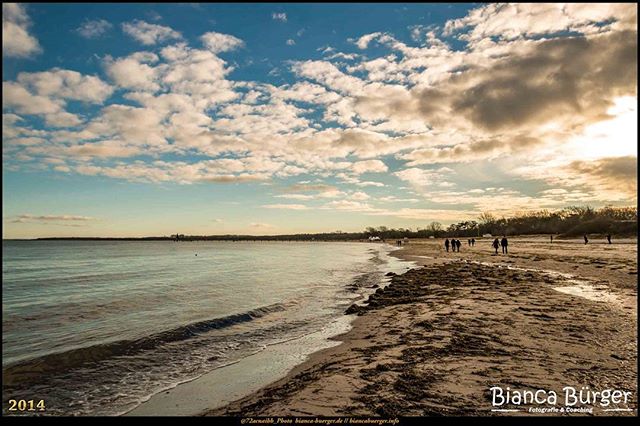 A tranquil beach scene with people walking along the shore under a partly cloudy sky, perfect for travel or relaxation themes.