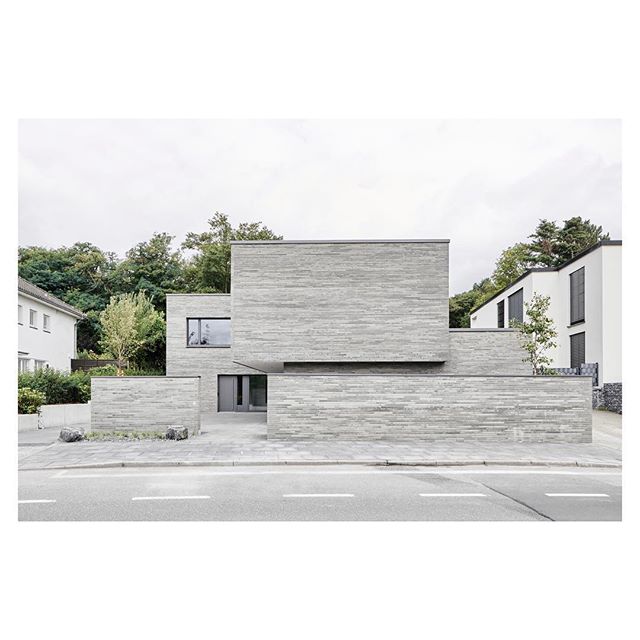 A modern, minimalist house with a grey brick exterior in a residential area.