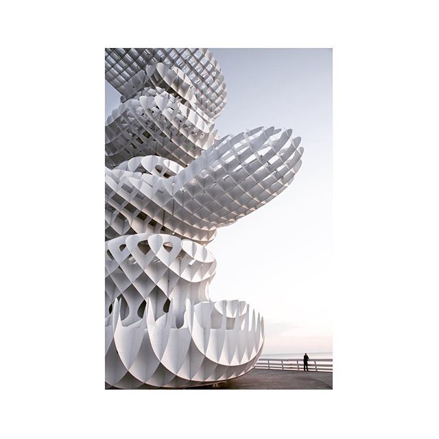 Abstract white sculpture near the sea with a person in the distance.