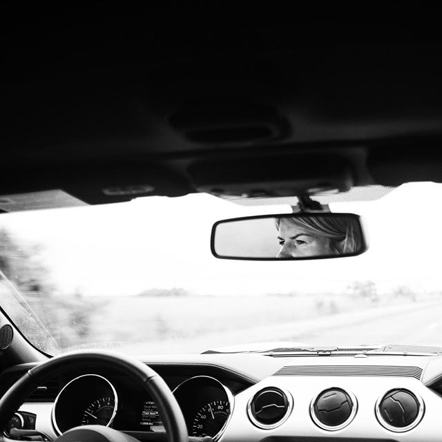 A woman's reflection in a car's rearview mirror while driving, creating a serene road trip scene.
