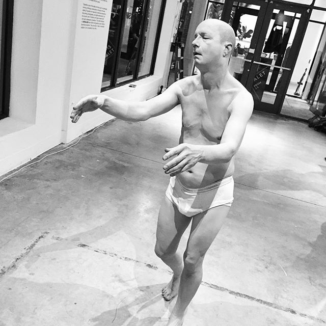 A man in underwear stands in a relaxed pose in a black and white studio shot.