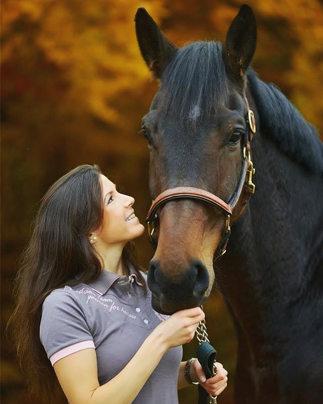 A woman smiles lovingly at her horse in a natural outdoor setting.