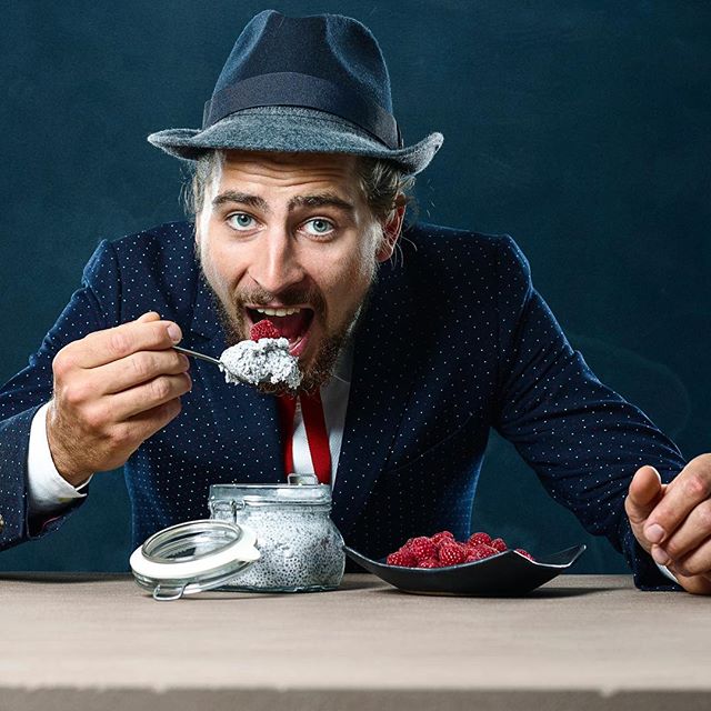 A cheerful man in a suit enjoys chia pudding with raspberries, promoting healthy eating.