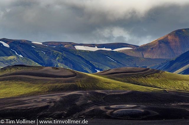 A scenic landscape featuring rolling hills and distant mountains under a cloudy sky in Iceland.