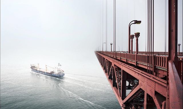 A cargo ship passes beneath a bridge shrouded in fog, creating a tranquil and scenic image.