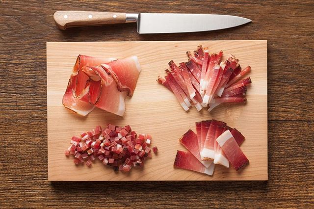 Overhead shot of different cuts of prosciutto on a cutting board with a knife.